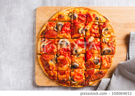 Close up of St. Louis Style pizza with bacon, mushrooms, tomatoes and peppers on a board top view 108064652