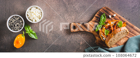 Bruschetta with cottage cheese, baked peppers and sesame seeds on a board top view web banner 108064672