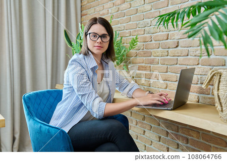 Portrait of young woman sitting at chair with laptop computer Portrait of young woman sitting at chair with laptop computer 108064766