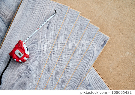 Measuring tape on wooden flooring planks for home renovation, construction works and interior design. Tape measure on samples of laminate boards with pattern and wood texture for flooring. Measuring tape on wooden flooring planks for home renovation, construction works and interior design. Tape measure on samples of laminate boards with pattern and wood texture for flooring. 108065421