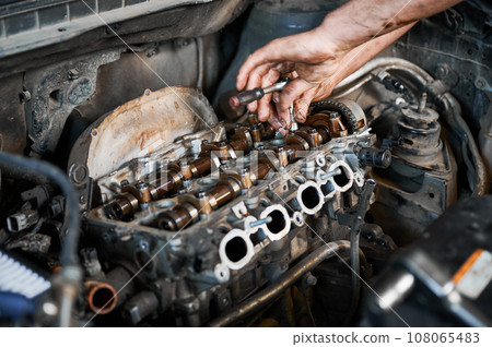 Close up of mechanic repairing car engine, working in garage, workshop, auto servicing center. Worker, repairman holding screwdriver. Concept of fixing car. 108065483