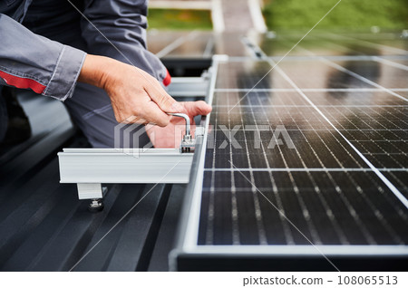 Professional installation of PV system on a roof. Close up view of competent engineer securing photovoltaic solar cell. Adjusting solar panel on top of house. Professional installation of PV system on a roof. Close up view of competent engineer securing photovoltaic solar cell. Adjusting solar panel on top of house. 108065513