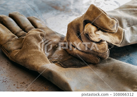 Old used gloves or welder's gloves lie on table and show gesture of denial from fingers. Concept of 108066312