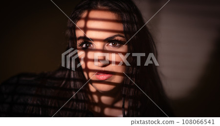 Beautiful photo os a young pretty woman effectfully lit through venetian blinds Beautiful photo os a young pretty woman effectfully lit through venetian blinds 108066541