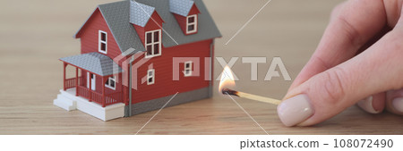Hand of woman holding match to burn house on wooden table 108072490