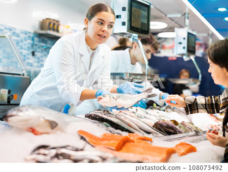 Woman seller of fish advises buyer to buy hake fresh fish 108073492