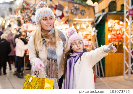 Smiling woman with tweenage daughter pointing to something while choosing decorations on traditional market 108073755