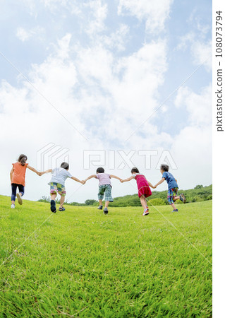 Rear view of elementary school students running up the hill in the park holding hands Rear view of elementary school students running up the hill in the park holding hands 108073794