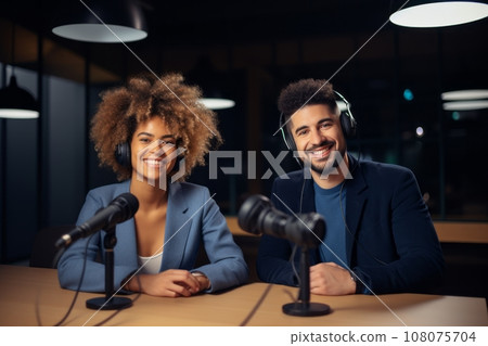 Beautiful multiethnic blogger couple hosting a podcast in a studio. Smiling woman and man wearing headphones sitting at a table with microphones and chatting cheerfully. Modern media technologies. Beautiful multiethnic blogger couple hosting a podcast in a studio. Smiling woman and man wearing headphones sitting at a table with microphones and chatting cheerfully. Modern media technologies. 108075704