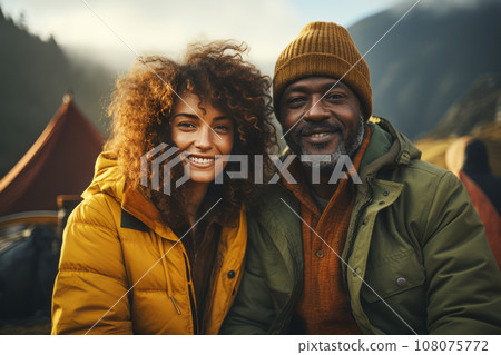 Portrait of happy multiethnic couple in the mountains against the backdrop of a tent camp. Young international family is engaged in a mountain hiking. Active lifestyle, tourism and vacation concept. 108075772