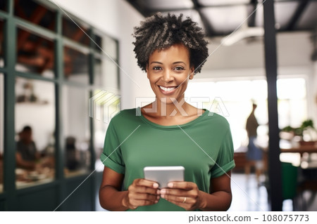 Portrait of cheerful African American woman in casual clothes holding a tablet or smartphone in cafe. Happy smiling young lady, successful entrepreneur or employee works online. Remote work concept. 108075773