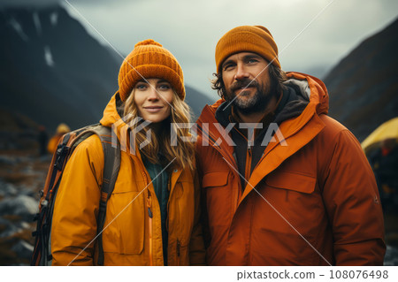 Portrait of happy couple in touristic outwear near the tent camp against the backdrop of picturesque mountain landscape. Caucasian family is engaged in a mountain hiking. Tourism and active lifestyle. 108076498