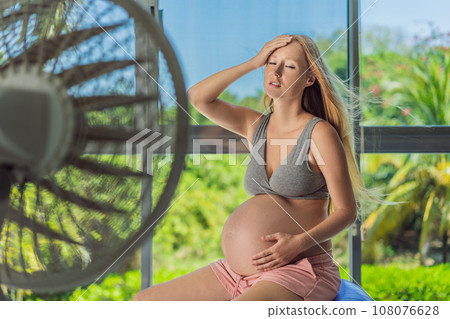 A pregnant woman seeks relief from an abnormal heatwave by using a fan, ensuring her comfort and well-being during sweltering conditions A pregnant woman seeks relief from an abnormal heatwave by using a fan, ensuring her comfort and well-being during sweltering conditions 108076628