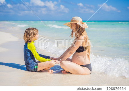 A radiant pregnant mother and her excited son share a tender moment on a serene, snow-white beach, celebrating family love amidst nature's beauty A radiant pregnant mother and her excited son share a tender moment on a serene, snow-white beach, celebrating family love amidst nature's beauty 108076634