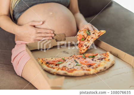 A pregnant woman enjoys a slice of pizza, savoring a moment of indulgence while satisfying her craving for a delightful, comforting treat. Excited Pregnant Young Lady Enjoying Pizza Holding Biting A pregnant woman enjoys a slice of pizza, savoring a moment of indulgence while satisfying her craving for a delightful, comforting treat. Excited Pregnant Young Lady Enjoying Pizza Holding Biting 108076635