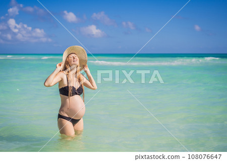 Radiant and expecting, a pregnant woman stands on a pristine snow-white tropical beach, celebrating the miracle of life against a backdrop of natural beauty 108076647