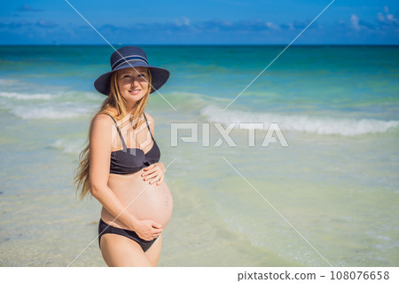 Radiant pregnant woman in a swimsuit, amid the stunning backdrop of a turquoise sea. Serene beauty of maternity by the shore Radiant pregnant woman in a swimsuit, amid the stunning backdrop of a turquoise sea. Serene beauty of maternity by the shore 108076658
