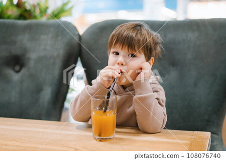 Little boy child drinks juice from a straw while sitting at a table in a cafe Little boy child drinks juice from a straw while sitting at a table in a cafe 108076740