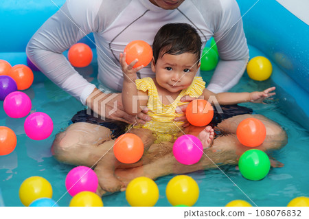 happy father and infant baby girl playing water with colorful plastic balls in inflatable pool happy father and infant baby girl playing water with colorful plastic balls in inflatable pool 108076832