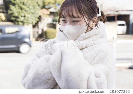 A woman wearing a mask and wearing a coat feeling cold outdoors 108077233