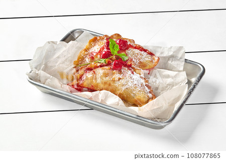 Puff pastry turnovers with cherry filling decorated with mint and powdered sugar 108077865