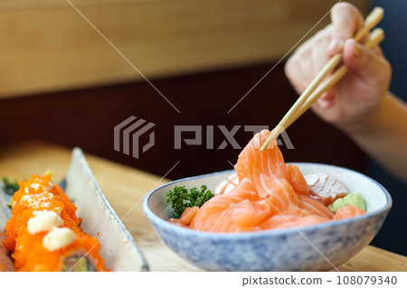Asian woman eating salmon slice sashimi with rice in Japanese restaurant Asian woman eating salmon slice sashimi with rice in Japanese restaurant 108079340