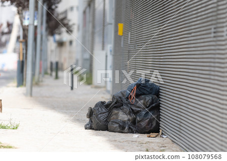Bags and trash beside a street wall. 108079568