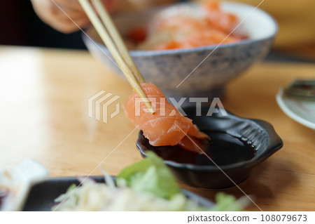 Salmon sashimi in chopsticks dipping with soy sauce Salmon sashimi in chopsticks dipping with soy sauce 108079673