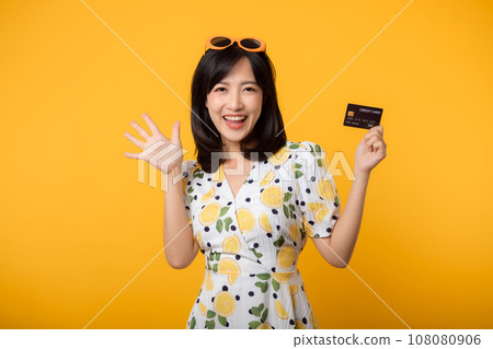 Portrait young asian woman happy smiling in springtime dress showing plastic credit card isolated on yellow background. Pay, money and purchase shopping payment concept. 108080906