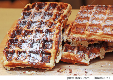 A lot of Freshly made belgian waffles sprinkled powdered sugar A lot of Freshly made belgian waffles sprinkled powdered sugar 108080935