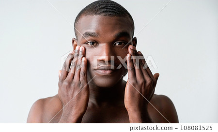 Man care. Facial treatment. Wrinkles skincare. Confident shirtless guy applying rejuvenation face skin cream under eyes isolated on white background. Man care. Facial treatment. Wrinkles skincare. Confident shirtless guy applying rejuvenation face skin cream under eyes isolated on white background. 108081525