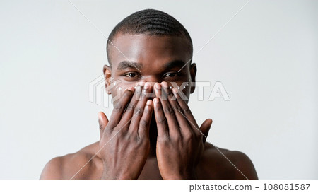 Male cosmetic. Skin moisturizing. Confident shirtless man applying face anti aging treatment skincare cream under eyes isolated on white background. 108081587