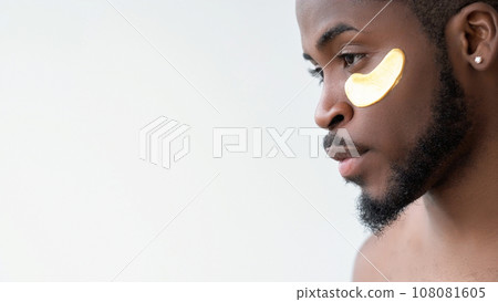 Male facial care. Skin rejuvenation. Handsome man with gold collagen gel eye patch on perfect radiant face isolated on white background empty space. Male facial care. Skin rejuvenation. Handsome man with gold collagen gel eye patch on perfect radiant face isolated on white background empty space. 108081605