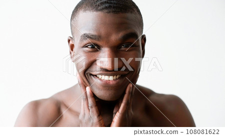 Man facial care. Morning hygiene. Amused happy handsome shirtless guy touching smooth soft moisturized face skin smiling isolated on white background. 108081622