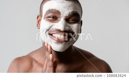 Man cosmetic. Facial mask. Confident satisfied guy enjoying applying face skin pore cleaning white clay smiling isolated on gray background. 108081624