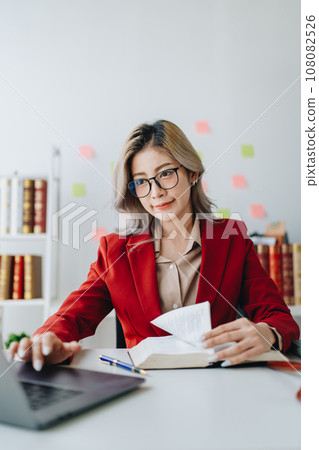 Portrait of a Asian woman lawyer studying lawsuit a for a client using computer laptop , documents to video conference before going to court 108082526
