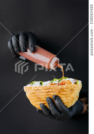 Cooks hand adding sauce to doner kebab through torn holes on black paper background. Street food Cooks hand adding sauce to doner kebab through torn holes on black paper background. Street food 108083488