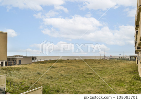 a grassy field with buildings in the background and blue sky above it, as seen from an apartment building on a sunny day 108083701