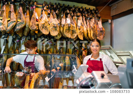 Young female and male vendors arranging jamon at counter in butcher shop 108083733