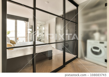 a bedroom with a large mirror on the wall, and a white bed in the room is reflected by the glass door a bedroom with a large mirror on the wall, and a white bed in the room is reflected by the glass door 108083743