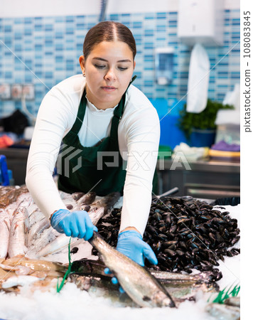 Female seller in apron shows hands fish trout on counter in supermarket 108083845