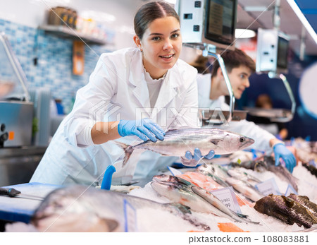 Positive saleswoman demonstrating bonito fish in fish store 108083881