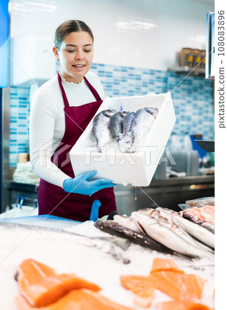 Smiling saleswoman holding dorada in fish store Smiling saleswoman holding dorada in fish store 108083896