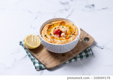 Roasted red pepper hummus in white bowl on white marble background 108084176