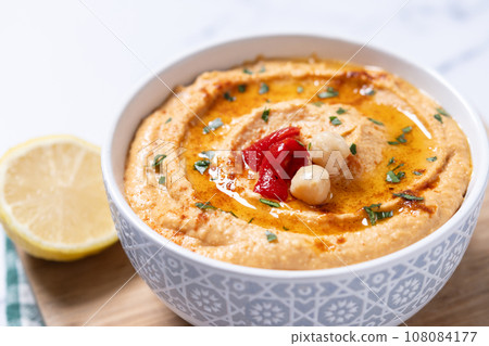 Roasted red pepper hummus in white bowl on white marble background Roasted red pepper hummus in white bowl on white marble background 108084177