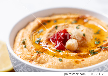 Roasted red pepper hummus in white bowl on white marble background 108084178