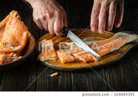 Chef's hands with knives while cutting or cleaning fresh fish on a cutting kitchen board before preparing a fish dish Chef's hands with knives while cutting or cleaning fresh fish on a cutting kitchen board before preparing a fish dish 108084391