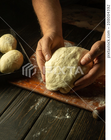 Male hands prepare dough for buns on the table close-up. Baker baking pies at home. Male hands prepare dough for buns on the table close-up. Baker baking pies at home. 108084392