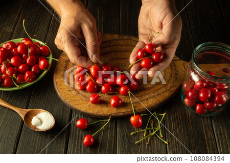The chef prepares a cherry drink in the kitchen. Cleaning and sorting cherries before filling with dill and adding sugar The chef prepares a cherry drink in the kitchen. Cleaning and sorting cherries before filling with dill and adding sugar 108084394