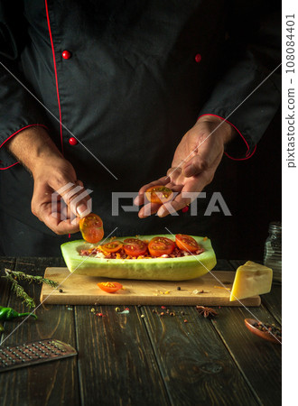 The cook prepares a stuffed zucchini boat on the kitchen table of the restaurant. Delicious lunch with national dish stuffed squash. Free space for menu or recipe The cook prepares a stuffed zucchini boat on the kitchen table of the restaurant. Delicious lunch with national dish stuffed squash. Free space for menu or recipe 108084401